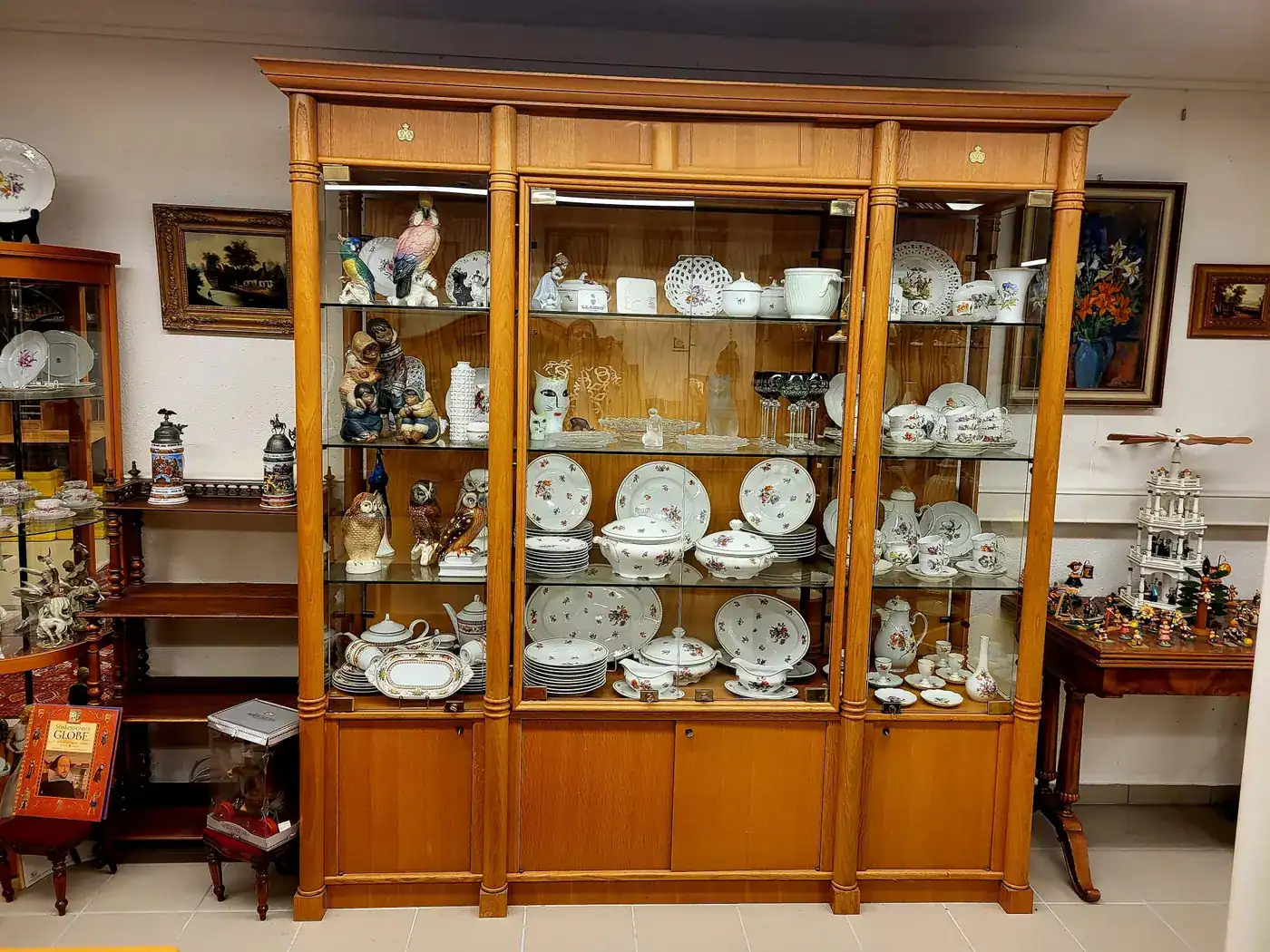 Große Vitrine mit Porzellanservicen, Figuren und Sammlerstücken im Ladengeschäft